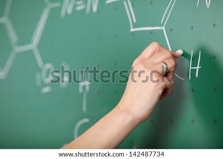 Student hands writing structural formula on the blackboard