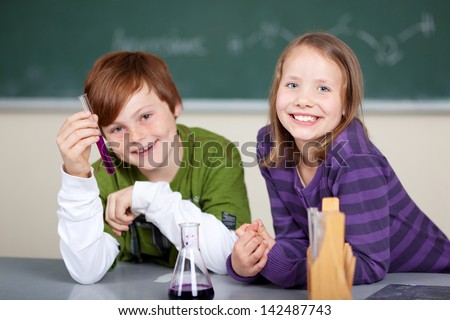Smiling kids having fun in the chemistry class with the little boy showing off a chemical reaction in a test tube