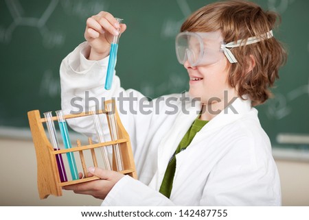 Young boy watching a chemical reaction standing wearing safety goggles and a lab coat and holding up a glass test tube