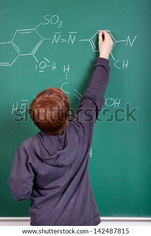 Young boy doing chemistry standing at the blackboard writing a formula on the board
