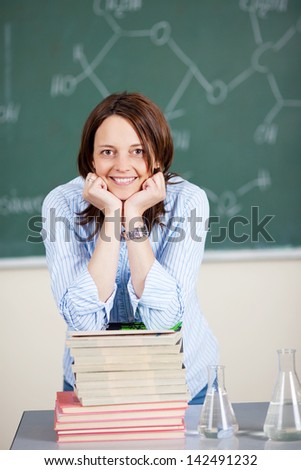 Smiling teacher laying her elbow on the stack of books