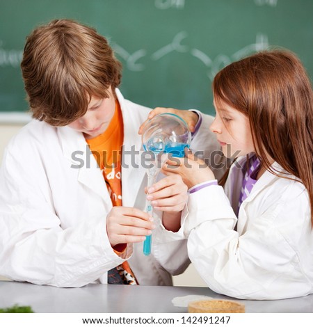 Young boy and girl in school learning chemistry working together as a team pouring liquids through a funnel into a test tube