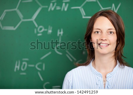 Head and shoulders portrait of an attractive female teacher in front of a blackboard with a chemical formula