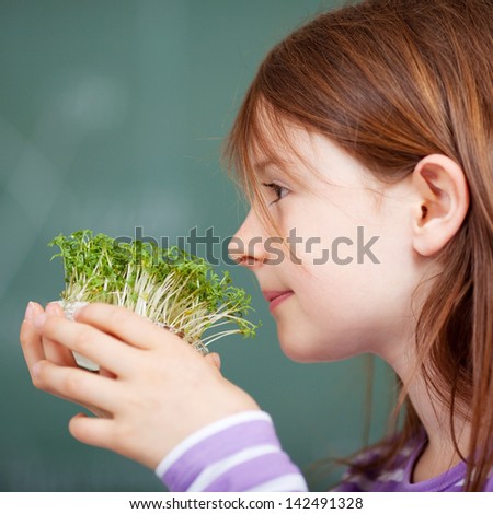 Closeup profile portrait of a cute young girl smelling freshly sprouted cress growing in a small container in her hands