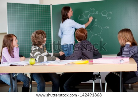 A teacher in chemistry class analyzing formulas on a blackboard
