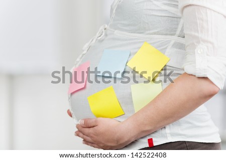 Side view of pregnant woman in office with post-it notes stuck on belly in office