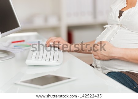 Midsection of pregnant woman with hand on belly using computer at table in house