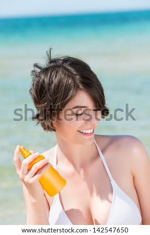 Young smiling woman spraying lotion in the beach