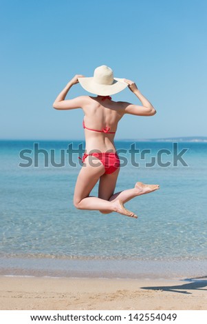 Rear view woman in red swimsuit jumping on beach, feeling freedom