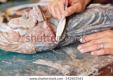 Detail shot of woman using putty knife on statue in workshop