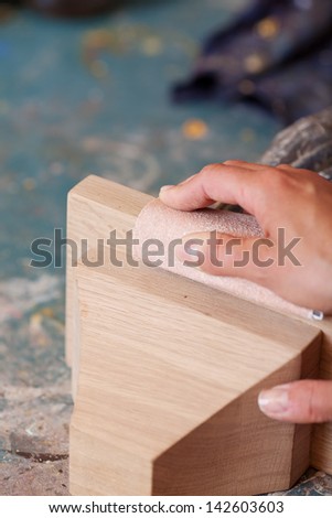 Womans hands polishing wood with sandpaper in workshop