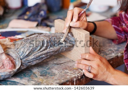 Closeup of woman using putty knife on statue in workshop