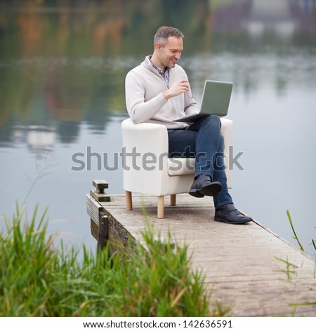 View on smiling mature man using laptop on pier
