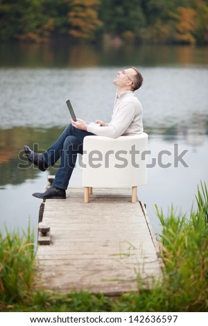 Full side view of happy excited mature man celebrating victory while using laptop on pier