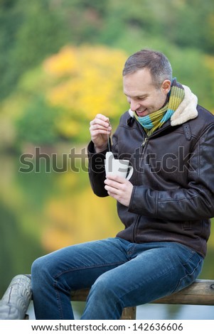 Happy mature man dipping tea bag in cup while sitting on fence