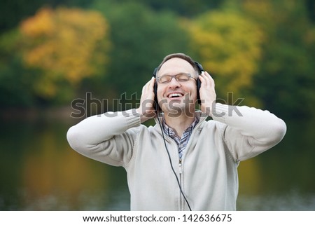 Happy mature man with eyes closed listening to music against lake