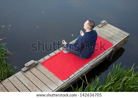High angle view of mature man meditating in lotus position on pier against lake