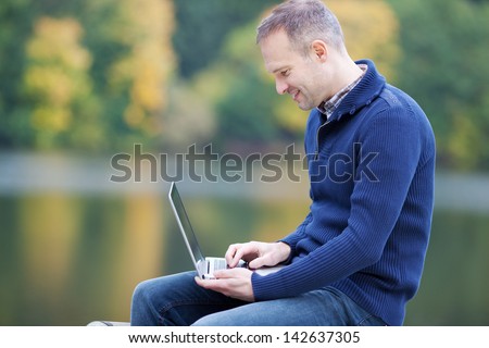 Side view of happy mature man using laptop against lake