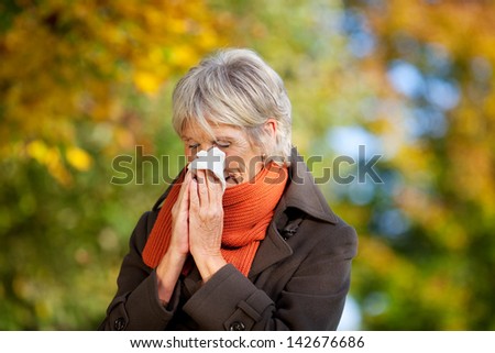 Senior woman in jacket suffering from cold in park