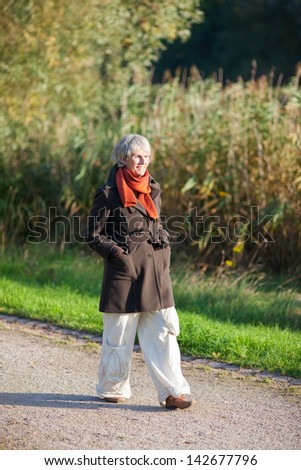 Full length senior woman in jacket walking in park
