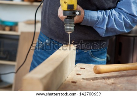 Midsection of senior male carpenter using electric drill at workbench