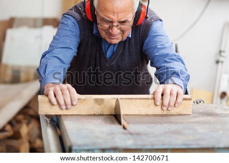 Senior man wearing ear protectors while using table saw for cutting wood at workbench
