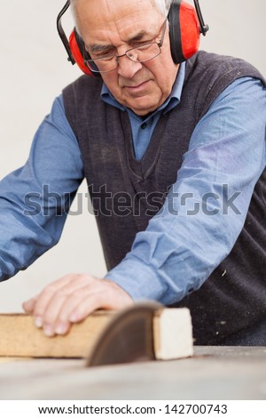 Senior man wearing ear protectors while using table saw for cutting wood at workshop