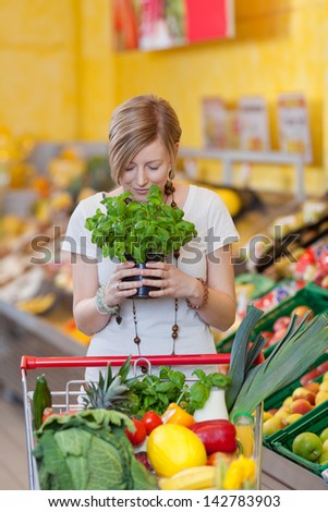 Young woman with shopping cart smelling basil plant in grocery store