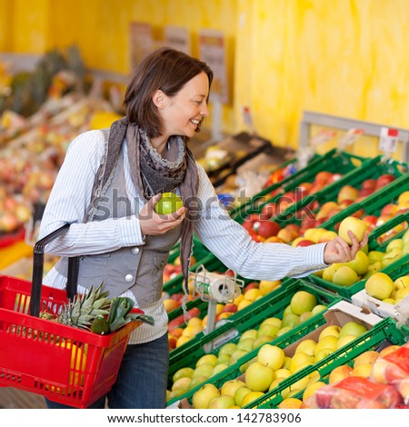 Happy mid adult woman with shopping basket choosing apples in grocery store