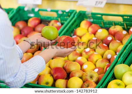 Female shopper purchasing apples in a supermarket holding one green and one red apple in each hand making her decision