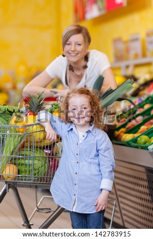 Beautiful mother and her little redhead daughter posing with a trolley full of fresh produce in a supermarket