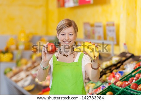 Image of a friendly saleswoman showing different fruits at the food counter in a supermarket.