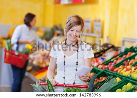 Woman With A Shopping List In A Supermarket Standing With Her Trolley In The Fresh Produce Section