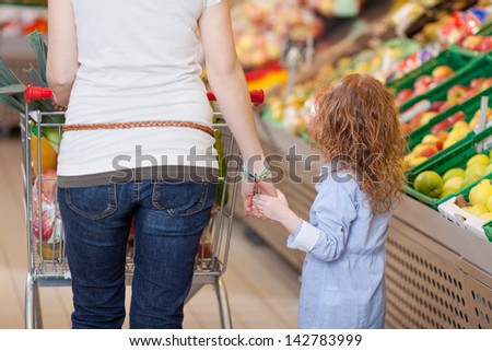 Image of a mother holding her kids hand inside the food department in a supermarket.