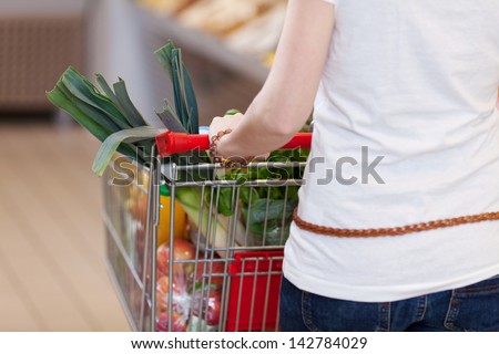 Woman pushing a shopping trolley filled with fresh fruit and vegetables for a healthy diet, closeup view