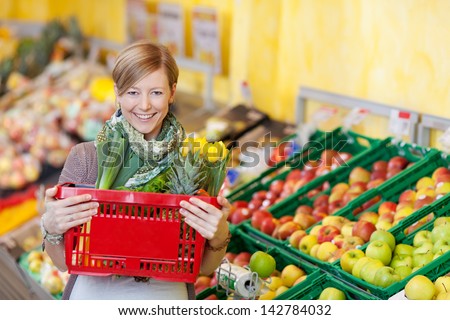 Portrait of happy young woman carrying shopping basket in grocery store