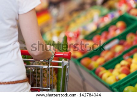Cropped image of young woman pushing shopping cart in grocery store