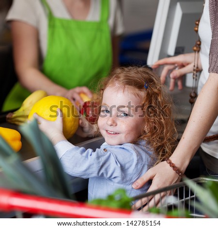 Image of a cute little girl smiling while buying a melon in the supermarket.