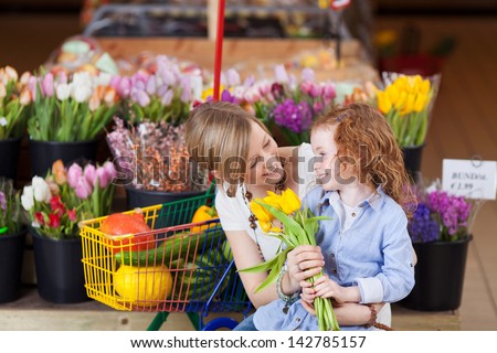 Smiling mother and little red headed daughter buying tulips crouching down together smiling and admiring the fresh flowers
