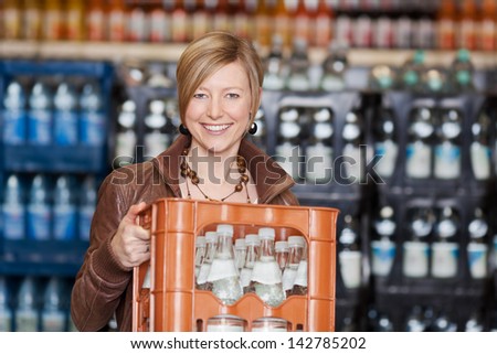 Portrait of happy woman carrying water bottles crate in supermarket