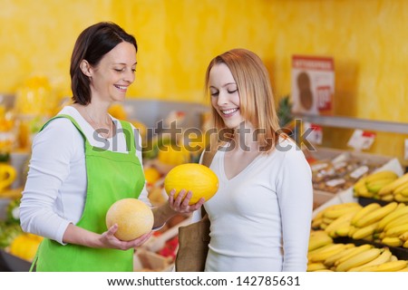 Friendly female worker assisting customer in choosing muskmelon at grocery store