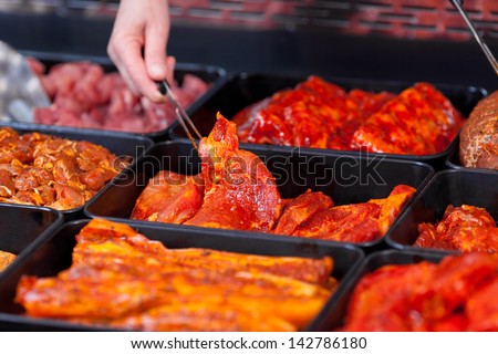 Selection of marinaded meat for grilling in a counter display in a supermarket with a female hand serving a slice with tongs