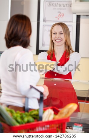 Happy saleswoman showing sliced cheese to female customer in grocery store
