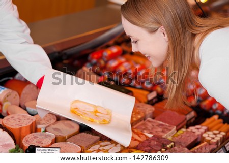 Happy young woman looking at sliced meat on butcher hand at supermarket