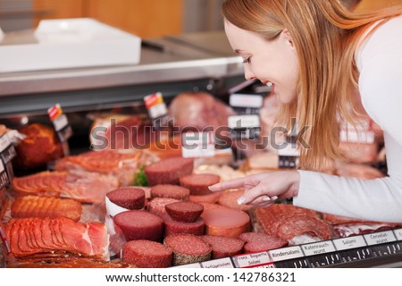 Happy young woman choosing meat from refrigerated section of supermarket