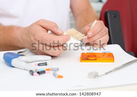 Midsection of doctor holding dental teeth shades samples at desk in clinic