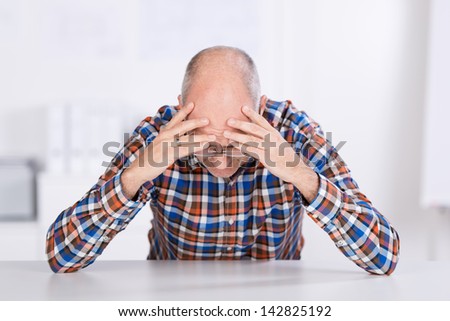 Stressed businessman with head in hands sitting at desk in office