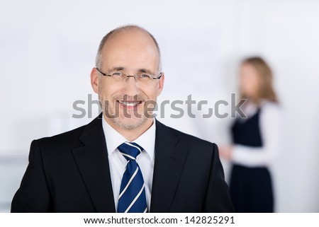 Portrait of confident businessman smiling with coworker in background at office