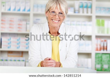 Portrait of confident female pharmacist smiling while leaning on counter in pharmacy