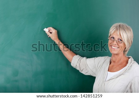 Senior school teacher giving a smile and writing on the blackboard inside the classroom.
